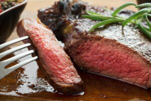 medium roast rib-eye steak on wooden plate with pepper and salt