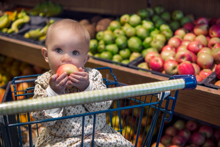 Cute baby in a shopping cart eating an apple