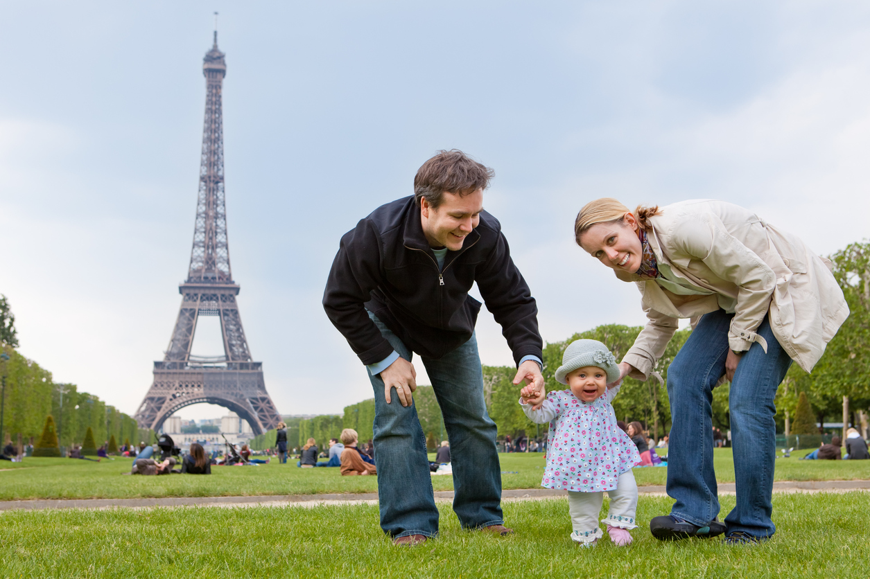 Young family with a baby visit Champ de Mars in front of the Eiffel tower in Paris.