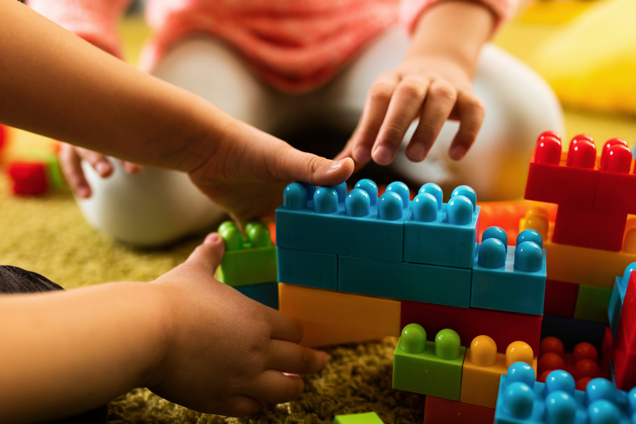 Close-up of two creative kids building something with plastic blocks on the floor.