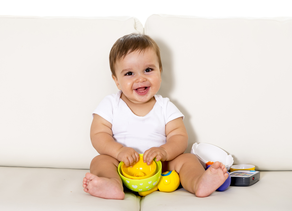 sweet cute little baby sitting on couch alone at home playing with toys happy and relaxed having fun smiling happy and laughing wearing white t-shirt and dippers