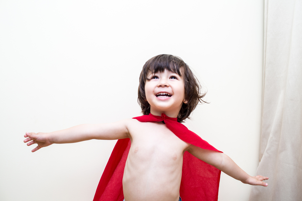 Little boy dressed in a red cape pretends to fly