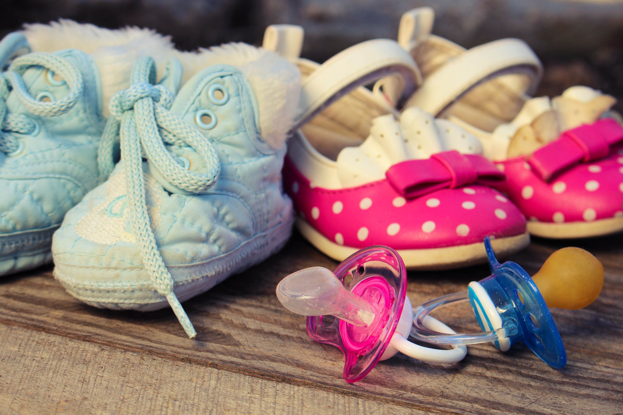 Baby shoes and pacifiers pink and blue on the old wooden background. Toned image.
