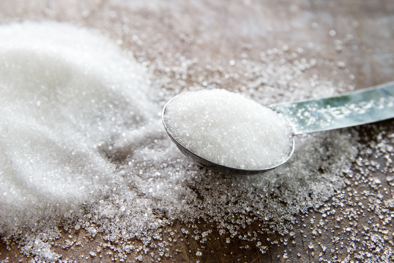 Close-up of granulated sugar in spoon and sugar pile on wooden