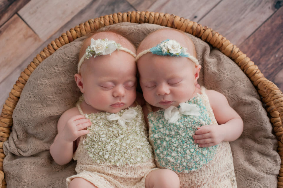 Seven week old fraternal, twin baby girls sleeping in a wicker basket. Shot in the studio on a rustic wood background.