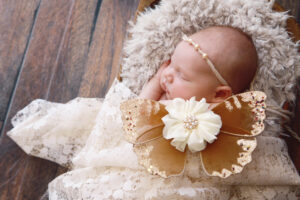 A newborn baby girl is sleeping in an antique bowl, wearing butterfly wings.