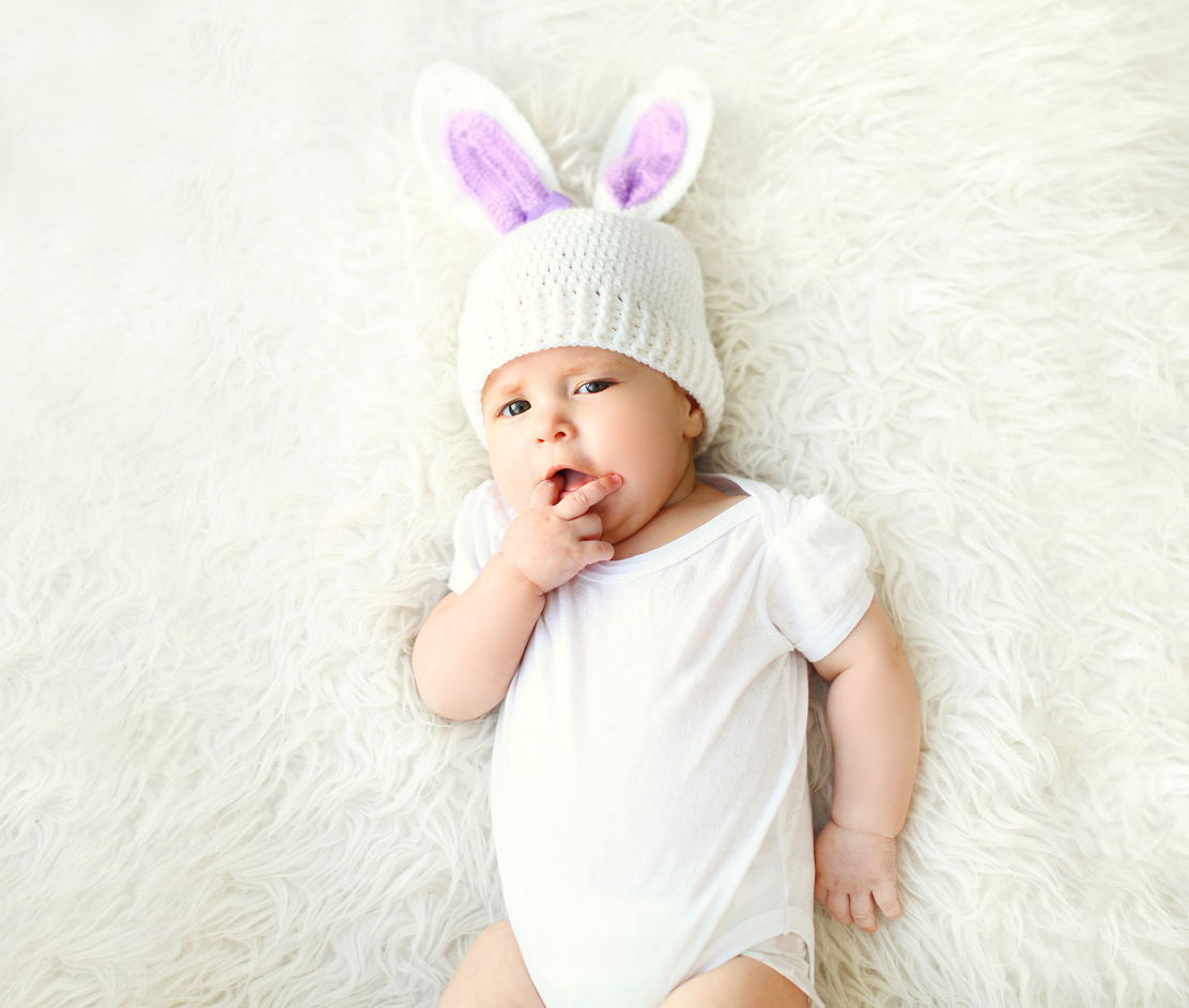 Sweet baby in knitted hat with a rabbit ears lying on bed, top view