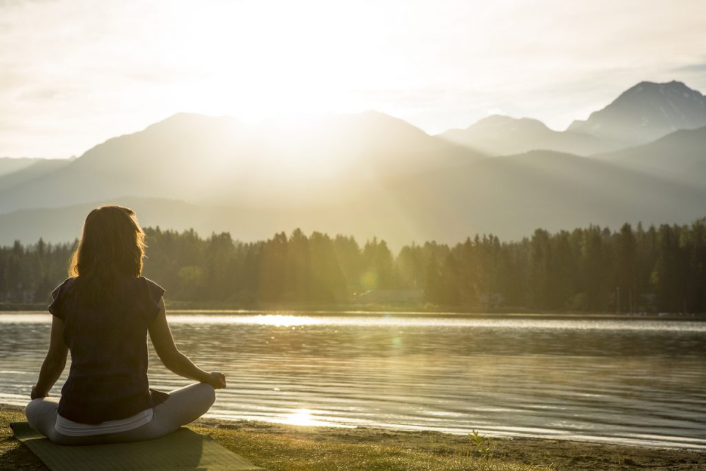 Meditation and yoga practice by lake at sunset or sunrise.