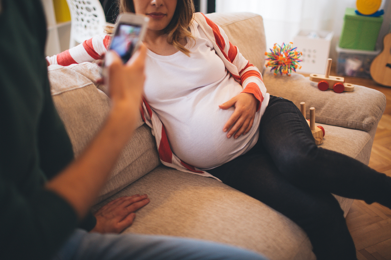 Young smiling couple, who is expecting a baby, taking a photos of a growing belly