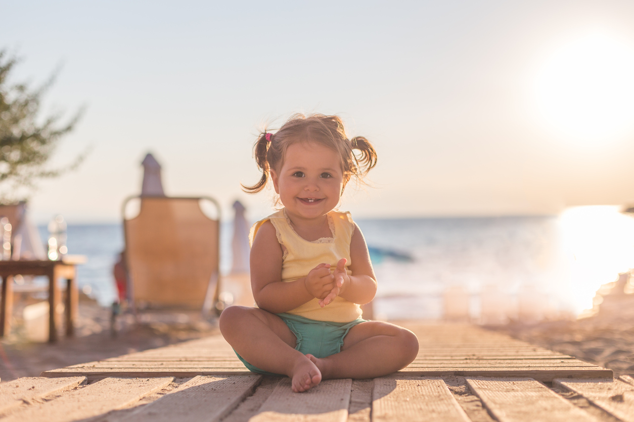 18 months old baby sitting and enjoying the sun , relaxing on a wooden boardwalk and discovering , happy baby - smiling and laughing