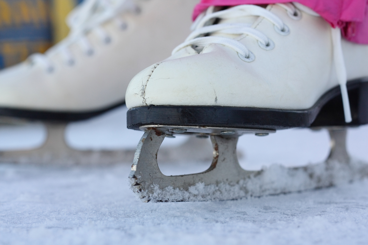 A girl wearing figure skates stands on an outdoor rink covered in a light layer of snow.