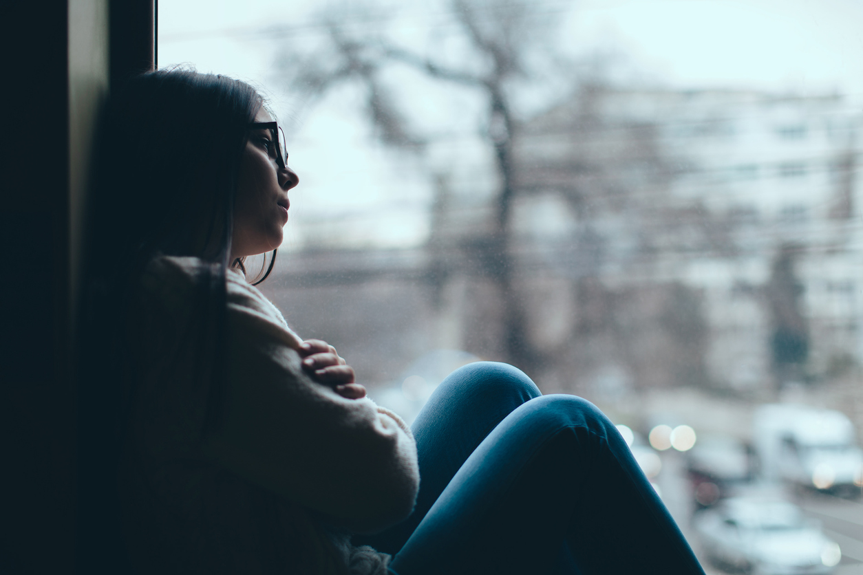 Silhouette of sad teenage girl looking out the window on a cold autumn day