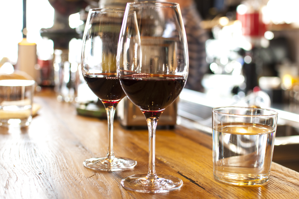 Two glasses of red wine and glass of water on the wooden bar counter