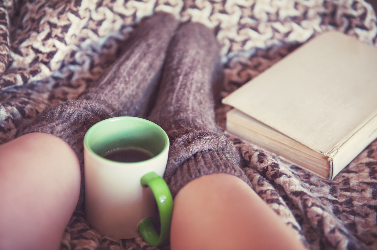 Woman legs in woolen socks with old book and a cup of tea