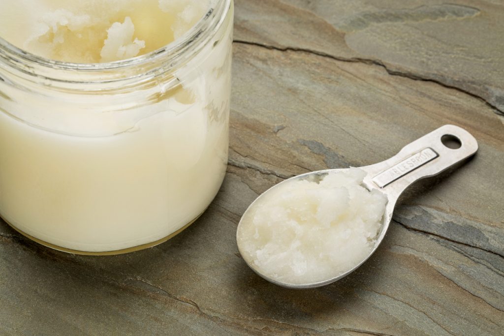 This is what to look for when buying coconut oil measuring tablespoon and glass jar coconut cooking oil on a slate rock background