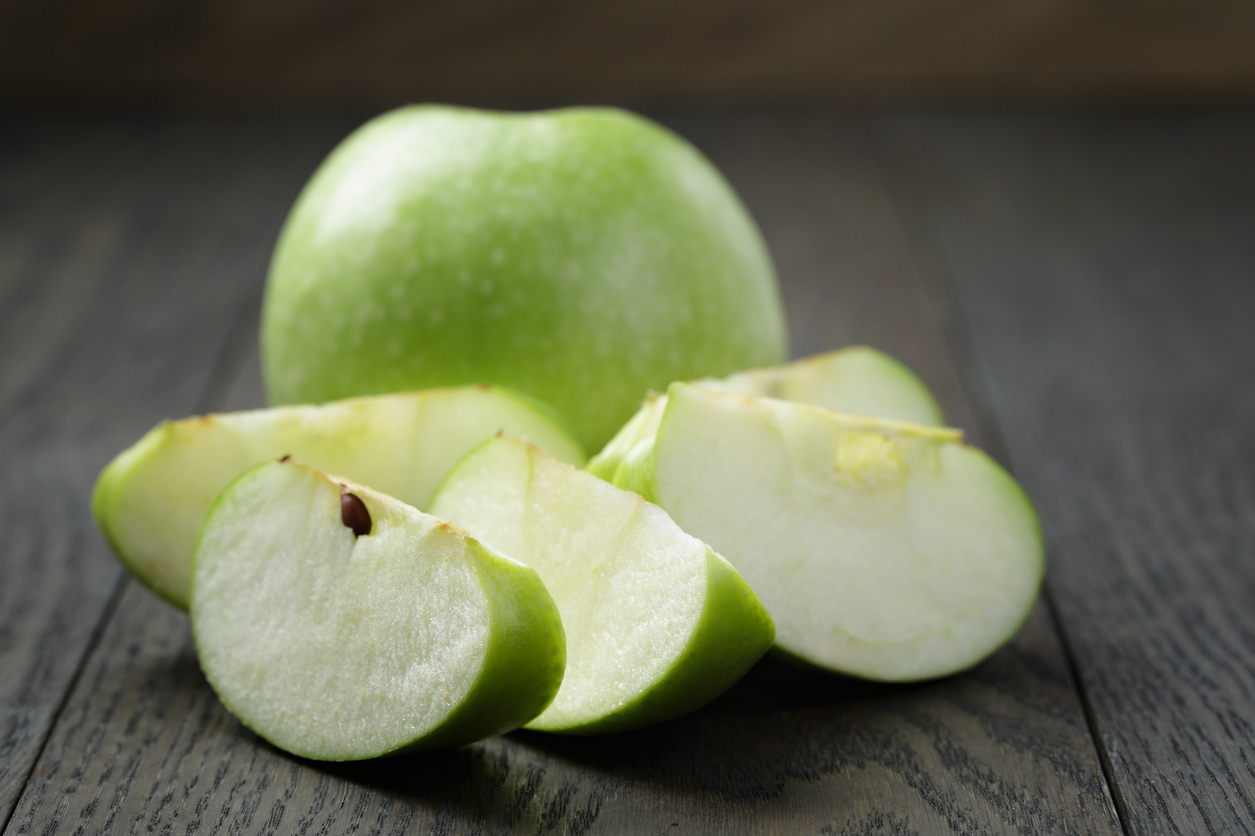 ripe green apples sliced on wood table, close up photo