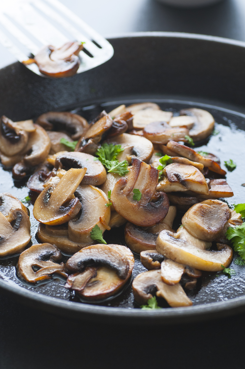 Butter fried sliced mushrooms with parsley in a pan.