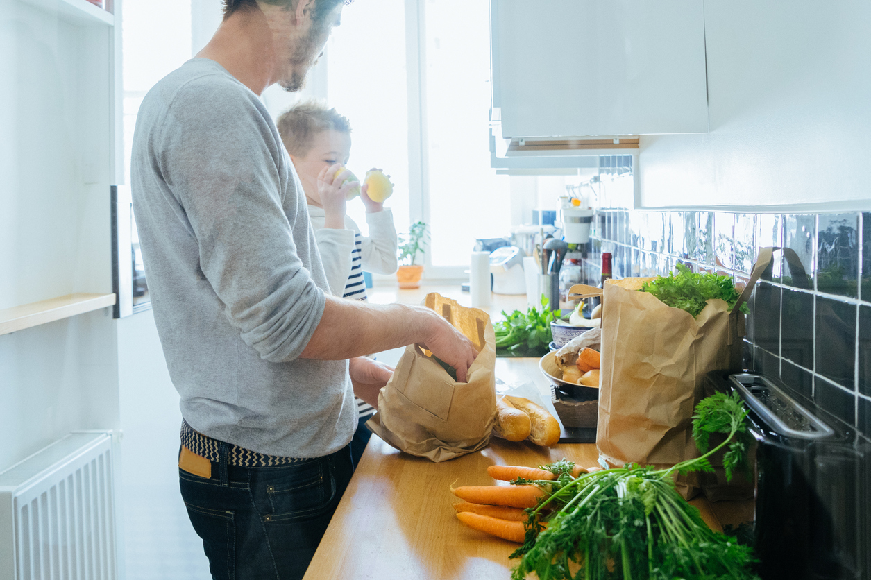 Happy father and son organizing groceries in the kitchen, paper bags full of healthy fresh food.