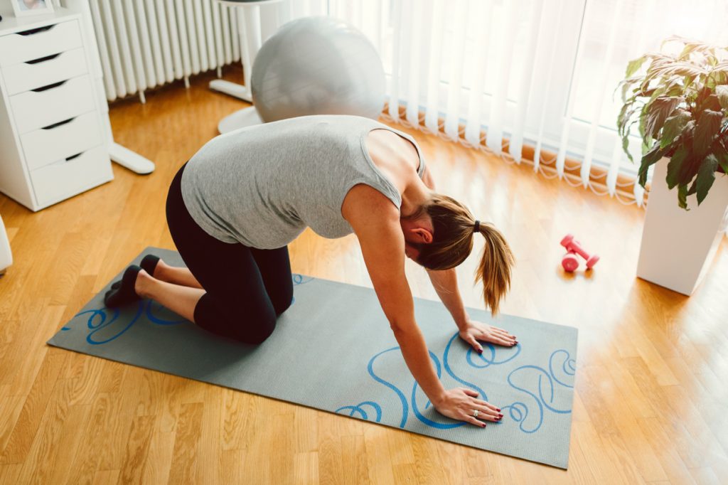 30 weeks pregnant woman exercising at home. Exercising on exercise mat and working stretching exercise.