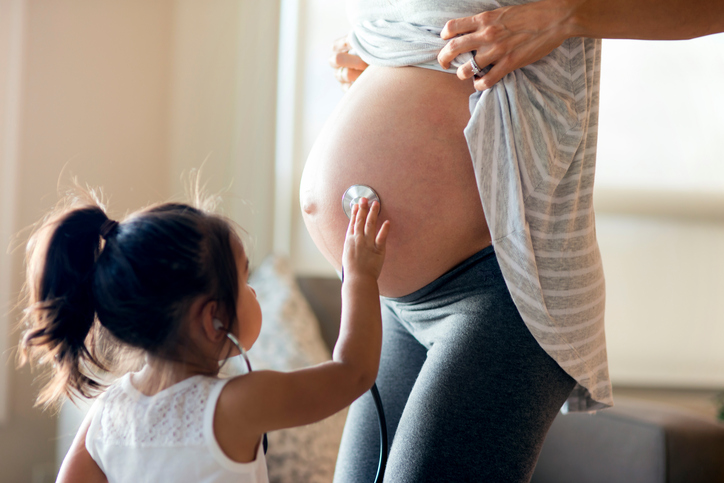 Young ethnic daughter holding stethescope up to moms pregnant belly