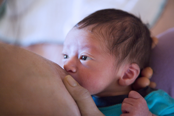 Newborn boy with large brown eyes staring at his mother as he breastfeeds