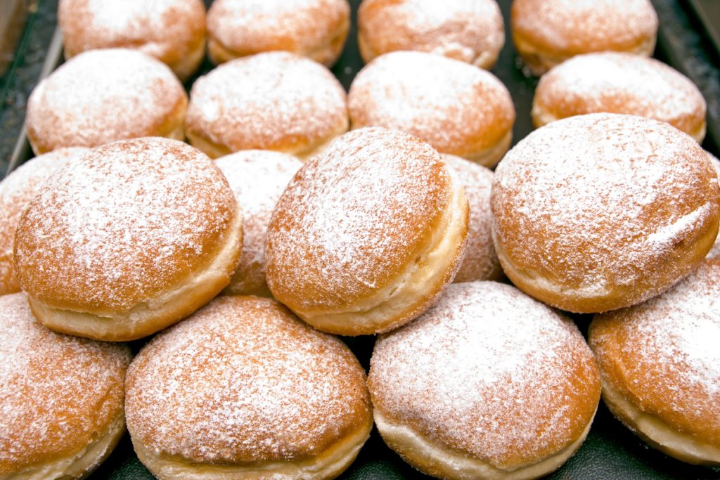 "Fresh baked German Jelly Doughnuts filled with strawberry jam or raspberry jam and dusted with powdered sugar. Full tray in a bakery counter display, delicious. Selective focus in foreground."