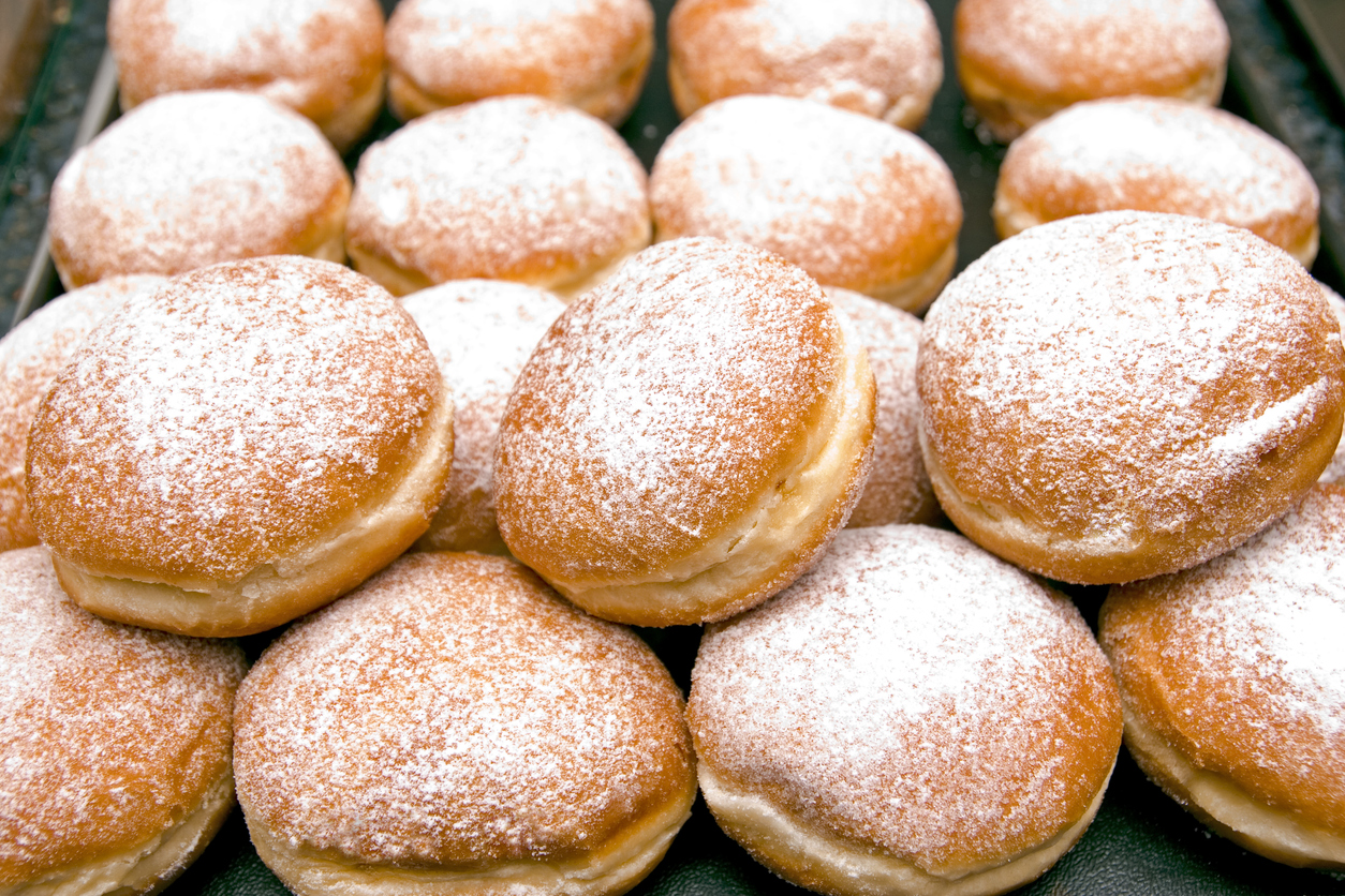 "Fresh baked German Jelly Doughnuts filled with strawberry jam or raspberry jam and dusted with powdered sugar. Full tray in a bakery counter display, delicious. Selective focus in foreground."