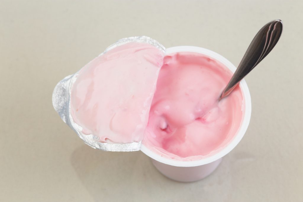 Opened cup of fruit yogurt with spoon in it close up photography.