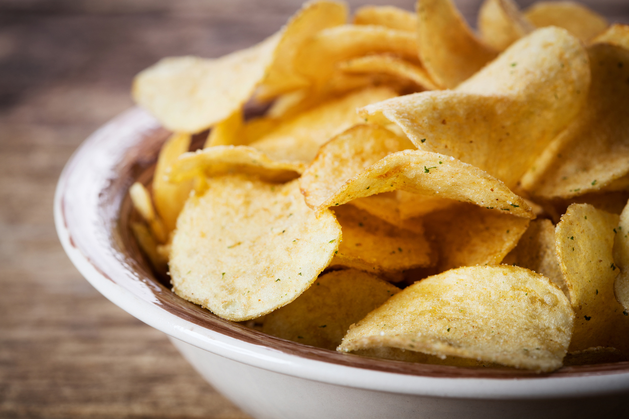 heap of potato chips in bowl on wooden background