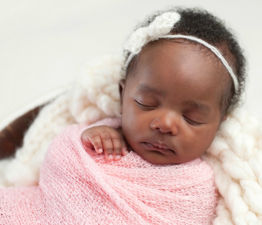 Portrait of a one month old, sleeping, newborn, baby girl. She is swaddled in pink and sleeping in a tiny bucket.