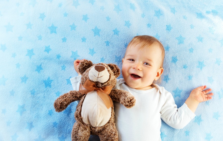 One year old baby lying in bed with a plush teddy bear