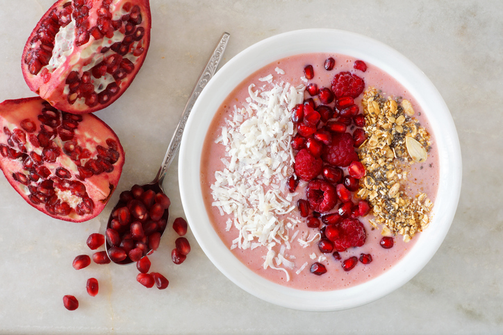 Smoothie bowl with pomegranates, raspberries, coconut, granola on marble