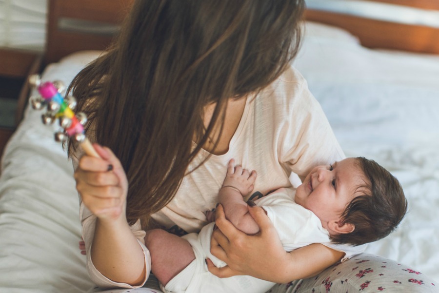 Mother is holding a baby girl and playing with a rattle