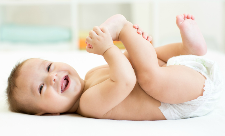 baby lying on white sheet and holding his legs