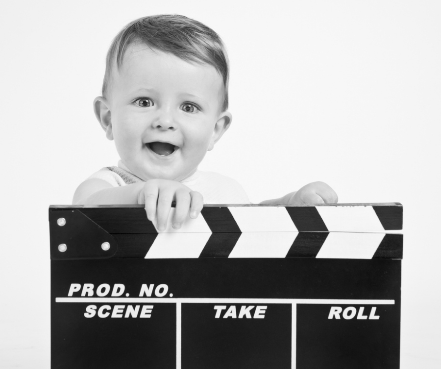 Adorable baby cine director with a film clap board over white background.