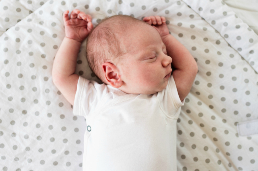 Cute little newborn baby boy lying on bed, sleeping, hands up. Close up.