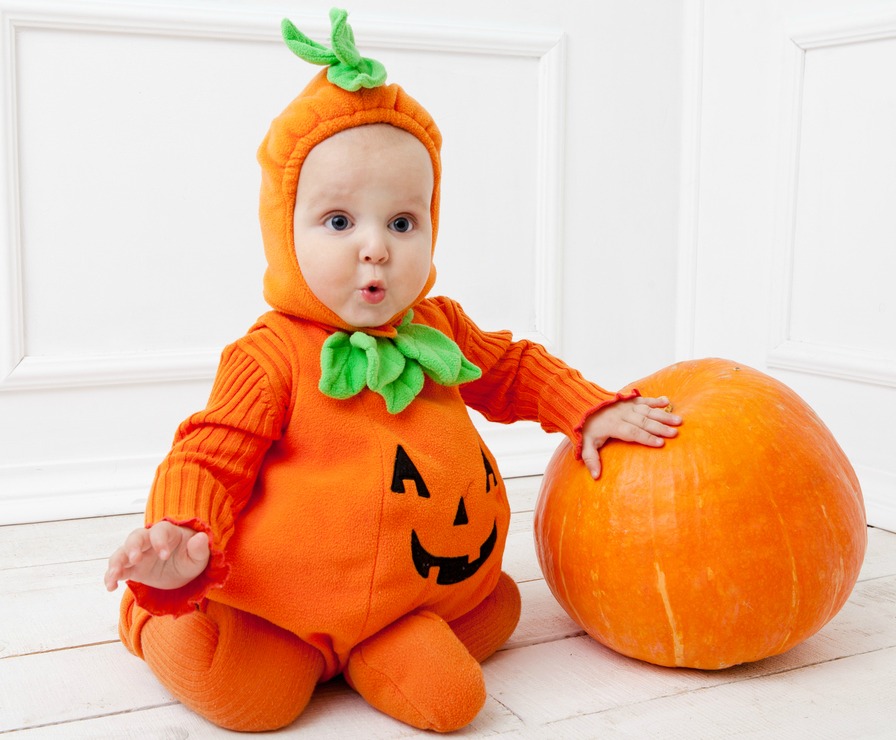 Child in pumpkin suit on white background with pumpkin