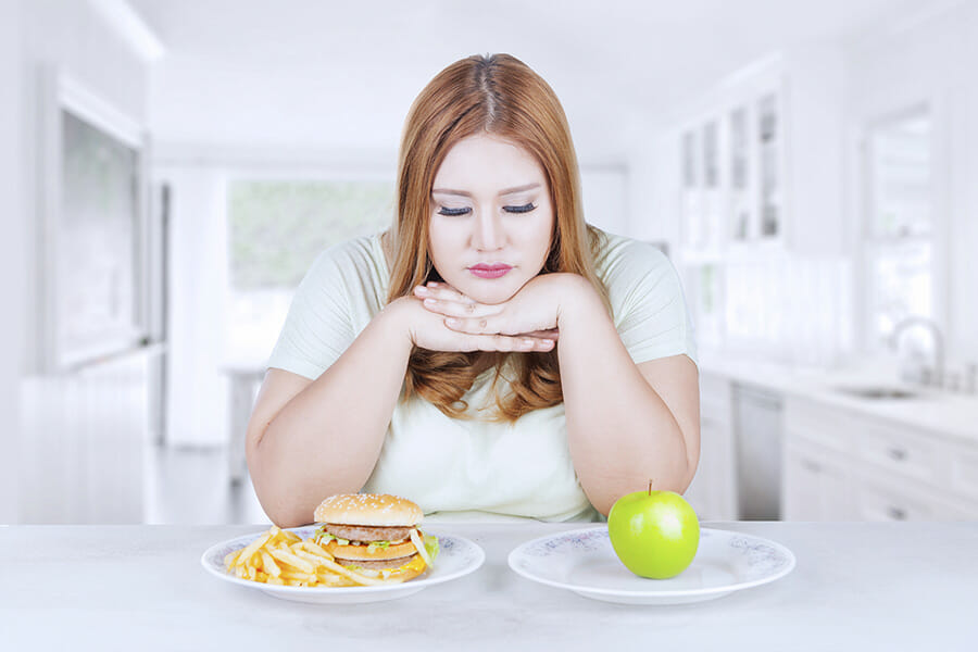 Emotional eating Confused woman choose apple or hamburger