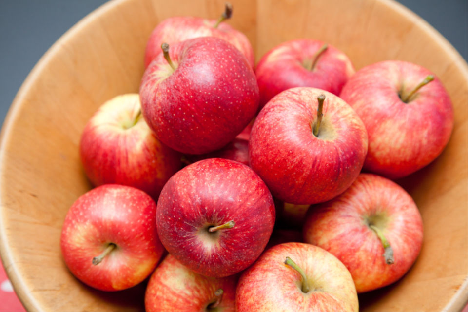 Red apples in a wooden bowl on a table with a heart symbol cloth.